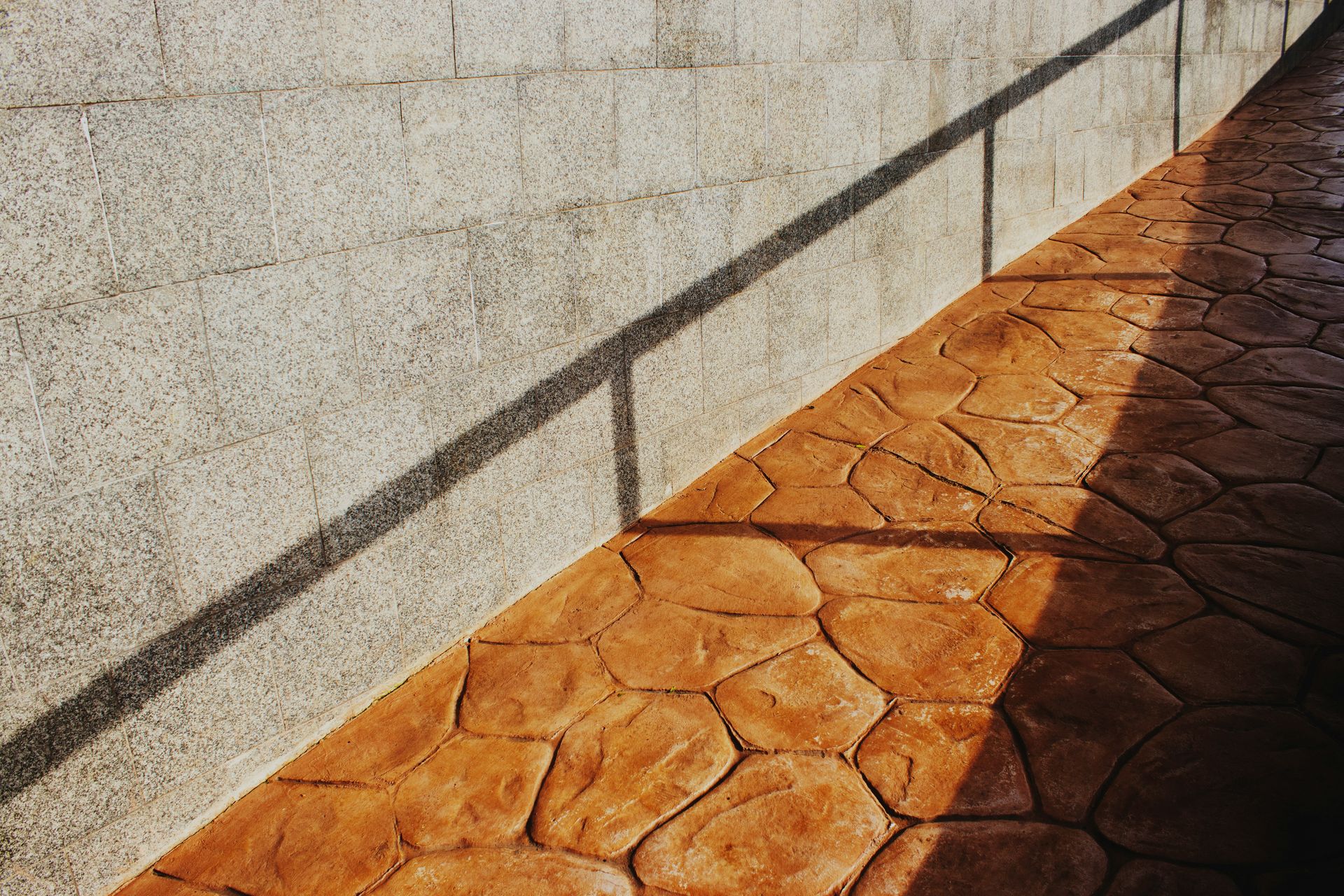 Shadows cast on a textured wall and patterned walkway.