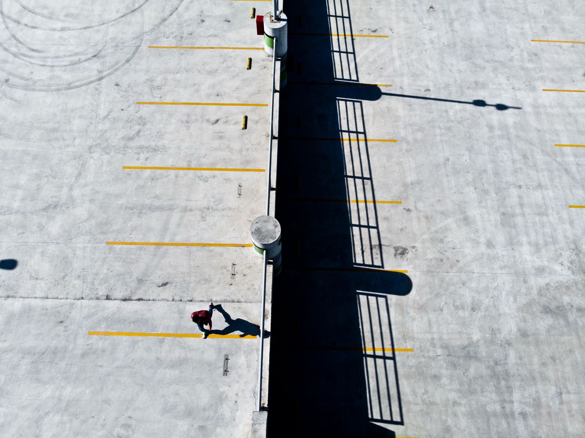 Drone shot of a person walking in an empty parking lot with long shadows.