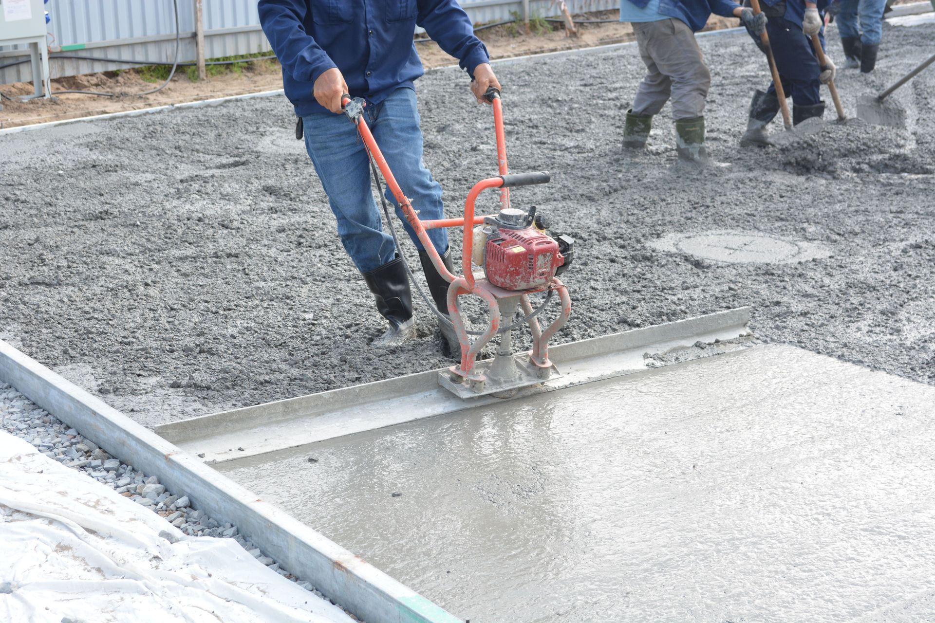 Team of construction workers using power tools to level freshly poured concrete on a building site.